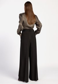 Pantalon noir à jambes larges taille haute, avec deux poches arrière, associé à un chemisier métallisé argenté à manches longues.