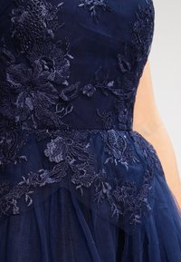 Mörkblå klänning med intrikata blommönster och lager av tyllkjol. Har texturerad tyg och en åtsittande boddesign.