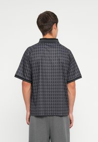 Kortermet polo skjorte i svart med diamantsamønster, med en kontrasterende svart krage og mansjetter, samt en avslappet passform.