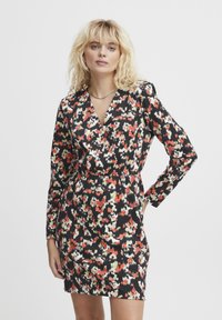 Robe noire à motif floral avec des teintes rouges, blanches et vertes. Manches longues, design croisé et silhouette ajustée. Texture lisse.