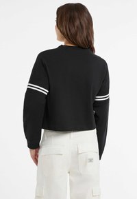 Felpa nera corta con strisce bianche sulle maniche, scollo rotondo e polsini a costine, abbinata a pantaloni cargo bianchi con tasche.