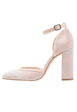 Chaussure à talon haut en daim rose blush avec une bride à la cheville, un bout pointu et un talon large et massif. Accents brillants à l'ouverture du bout.