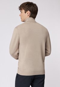 Beige gestrickter Pullover mit hohem Kragen und gerippten Details am Saum und an den Manschetten. Merkmale ein einfaches, strukturiertes Material mit einer taillierten Silhouette.