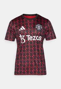 Punainen ja musta lyhythihainen pelipaita, jossa on geometrinen kuvio, pyöreä kaula-aukko, Adidas-logo ja etupuolella sponsorin teksti "Tezas".