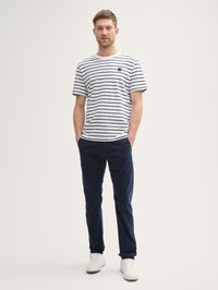 T-shirt blanche rayée avec des lignes navy, col rond et petite patch sur la poitrine. Associé avec un pantalon en velours côtelé navy et des baskets blanches.