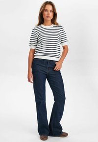 Svītrains adīts džemperis baltā un tumši zilā krāsā, ar apaļu kakla izgriezumu un īsām pūkainām piedurknēm. Pāris ar tumšu džinsu platām biksēm un brūnām plakanu apavu kurpēm.