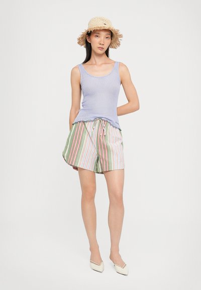 Débardeur violet à côtes, short rayé vert et blanc avec des accents roses, et chapeau en paille avec un bord effiloché. Chaussures pointues blanches.
