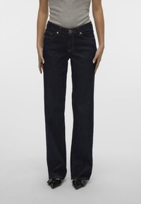 Los pantalones denim azul oscuro presentan un corte de pierna recta, diseño de cinco bolsillos y costuras en contraste. Cierre frontal con botón y cremallera.