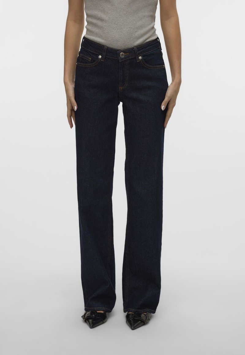 Los pantalones denim azul oscuro presentan un corte de pierna recta, diseño de cinco bolsillos y costuras en contraste. Cierre frontal con botón y cremallera.