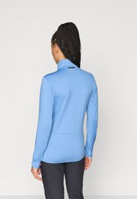 Ljusblå långärmad topp med hög krage, texturerad tyg och en figurnära design, med en liten logotypdetalj på baksidan.