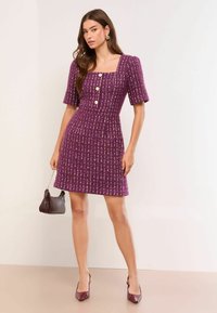 Abito a maglia viola con scollo quadrato, maniche corte a sbuffo e dettaglio con tre bottoni. Il tessuto presenta una texture a righe verticali.