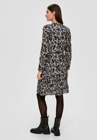 Leopardenmusterkleid in Grau und Schwarz, mit langen Ärmeln, gestuftem Rüschensaum, gerafftem Taillenbereich und kombiniert mit schwarzen Ankle-Boots.