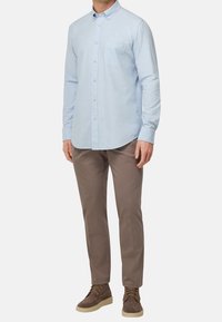 Ljusblå långärmad skjorta med knappar och bröstficka, kombinerad med beige byxor och bruna mockaskor.