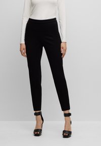 Zwarte fitted broek met een gladde textuur, een hoge tailleband en enkellange pasvorm, gecombineerd met zwarte sandaaltjes met hoge hakken.