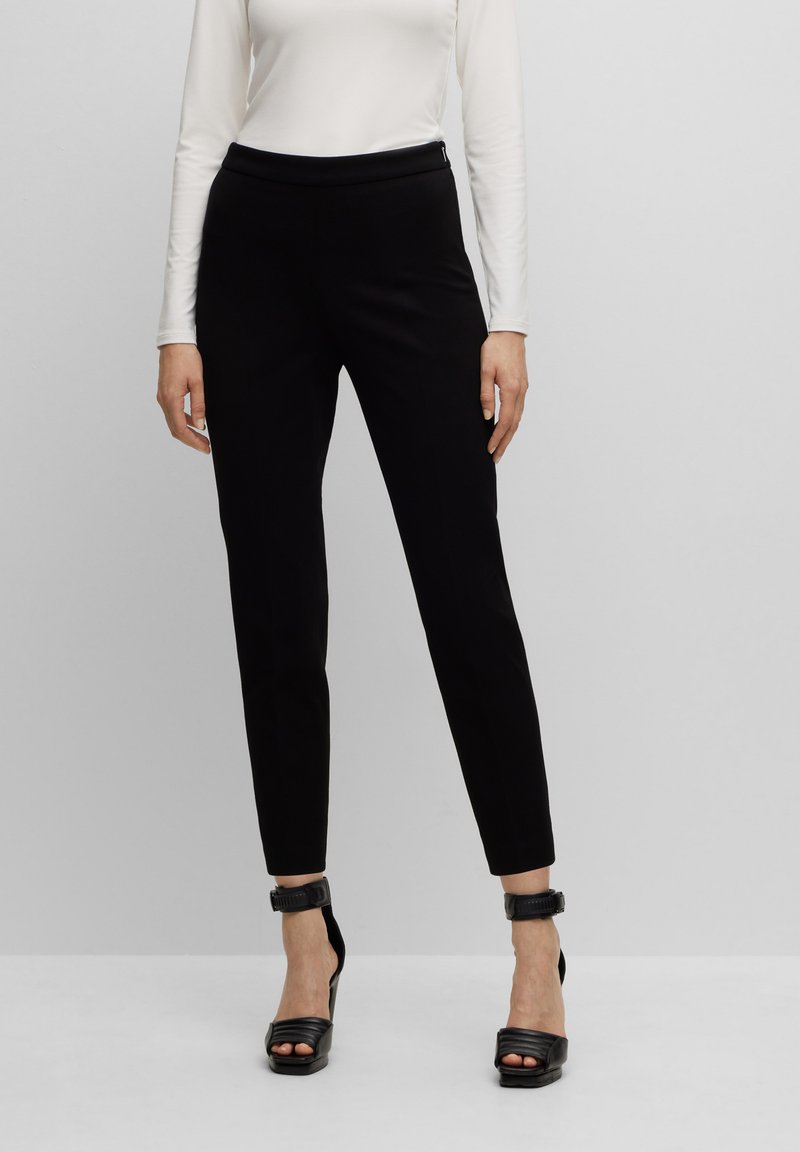 Zwarte fitted broek met een gladde textuur, een hoge tailleband en enkellange pasvorm, gecombineerd met zwarte sandaaltjes met hoge hakken.
