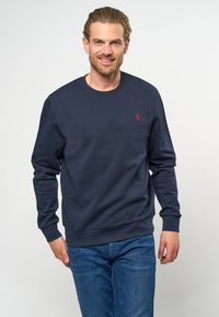 Marineblauwe crewneck sweatshirt gemaakt van zachte stof, met lange mouwen en een klein rood logo op de borst.
