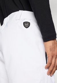 Άσπρα αθλητικά σορτς με ομαλή υφή, ρυθμιζόμενο μέση και μαύρη ετικέτα λογότυπου EA7 στο ισχίο. Ορατή πλαϊνή τσέπη.