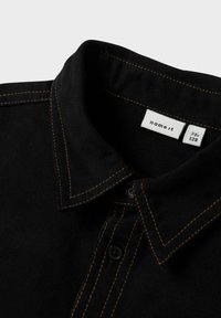 Camisa negra con costuras naranjas, diseño con cuello y cierre de botones. Presenta una tela texturizada y una etiqueta que indica la talla 7-8 años.