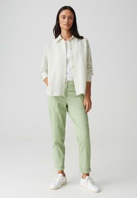 Camicia verde chiaro a maniche lunghe con righe verticali sopra una maglietta bianca, abbinata a pantaloni verde chiaro e sneakers bianche.