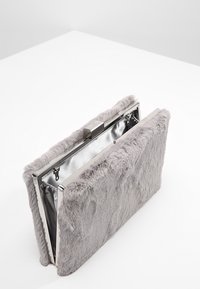 Pochette grise en fausse fourrure de forme rectangulaire, avec quincaillerie argentée et intérieur métallique. Dispose d'une fermeture à clip et d'une surface texturée.
