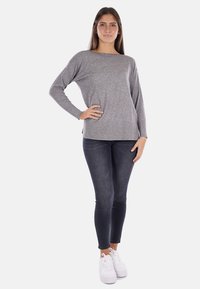 Maglia grigia a maniche lunghe con vestibilità rilassata e scollatura ampia, abbinata a jeans scuri e sneakers bianche, con una texture liscia.