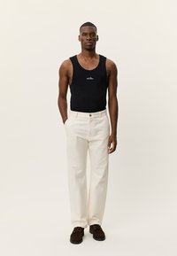 Μαύρο βαμβακερό αμάνικο με λευκό κεντημένο λογότυπο, σε συνδυασμό με ψηλόμεσα, εκρού, παντελόνια ίσιας γραμμής και καφέ παπούτσια με κορδόνια.