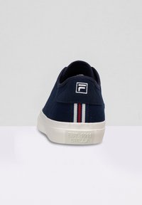Sneaker in tela navy con suola bianca, con logo sul tallone e strisce rosse e bianche sul retro. Tessuto testurizzato e design minimalista.
