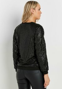 Felpa nera con paillettes, caratterizzata da un motivo testurizzato, orlo a coste e maniche lunghe. Presenta un collo tondo e una vestibilità ampia.