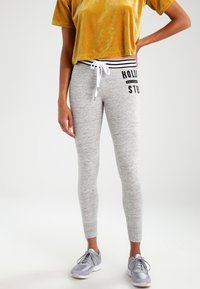 Šedé elastické legíny s tkaničkovým pasem a černým potiskem. Vydání s krátkým, žlutým, sametovým topem. Šedé sportovní boty.