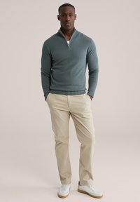 Pull-over bleu clair avec une fermeture éclair au quart, tissu texturé, associé à un pantalon beige et des baskets blanches. Design simple et épuré.