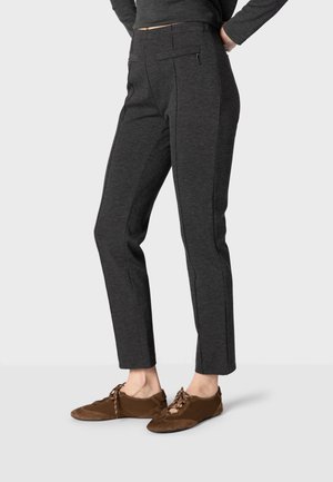 Pantalon slim gris foncé avec fermeture éclair à l'avant et poches, porté avec des chaussures marron à lacets, montré de la taille aux pieds sur un fond uni.