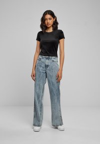 Zwart strak aangesloten T-shirt, lichtblauwe wijde jeans, witte sneakers. Eenvoudig ontwerp, gladde textuur, casual stijl, minimale accenten, geen patronen.