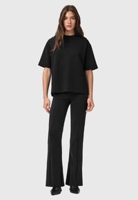 Zwarte oversized t-shirt met korte mouwen, gecombineerd met zwarte flared broek. Beide kledingstukken hebben een gladde textuur en een ontspannen fit.
