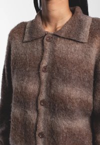 Cardigan in lana marrone con davanti abbottonato, collo e superficie morbida e lavorata con sfumature degradanti dal marrone chiaro al marrone scuro.