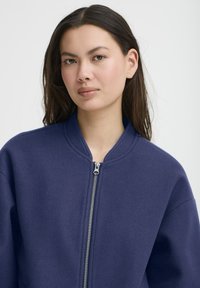 Jūras spēku bumbiera jakas ar gludu tekstūru, ribotu apkakli un pilnu priekšējo rāvējslēdzēju. Apģērbs ar nobīdītām plecu šuvēm un brīvu piegriezumu.