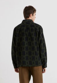 Camicia a maniche lunghe in velluto a coste verde scuro con un motivo geometrico circolare, caratterizzata da un taglio dritto e chiusura a bottone sul colletto.