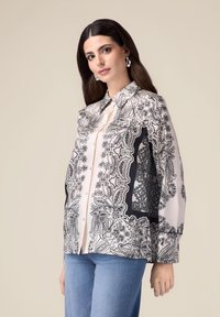 Blouse à manches longues en tissu doux, ornée d'un motif paisley noir et blanc détaillé, avec un système de fermeture à boutons et un col classique.