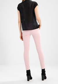 Top negro de mangas cortas con pliegues combinado con jeans skinny rosa claro y botas de tacón negro hasta el tobillo, mostrando una silueta elegante.