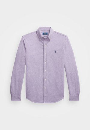 Chemise boutonnée à manches longues de couleur violet clair, en tissu de coton, avec un col classique et un petit logo brodé sur la poitrine gauche.