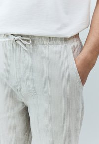 Pantalon gris clair à rayures avec une taille élastique et un cordon de serrage, doté de poches latérales et d'un tissu doux et texturé.