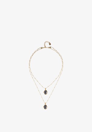 Collar de cadena de oro de doble capa con dos colgantes ovalados de piedras preciosas oscuras de diferentes longitudes sobre un fondo blanco.