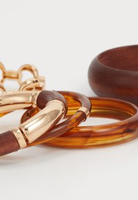 Dažādas bangle aproces: divas dzintara krāsas sveķu, viena brūna koka un viena zelta toņa metāla akcenta detaļa. Gludas un spīdīgas tekstūras, atšķirīgi platumi.