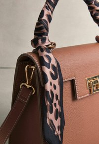 Brązowa skórzana torebka o teksturowanej powierzchni, z złotym zapięciem i jedwabną rączką w wzór czarno-różowej pantery.