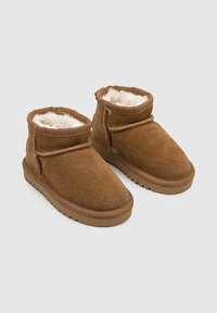 Botas de tobillo de ante marrón con un suave forro de piel sintética color crema, puntera redonda y suela de goma plana. Presenta un puño doblado.