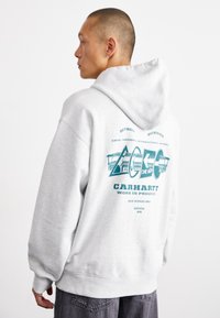 Gray hooded sweatshirt features a large graphic on the back with teal accents, showcasing "CARHARTT WORK IN PROGRESS" text and various indicators.