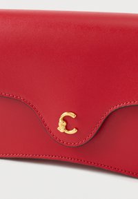 Portafoglio in pelle rossa con bordo curvo, logo dorato in rilievo e cuciture a contrasto. Texture liscia, design minimalista.