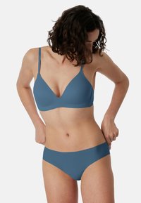 Modrá bezešvá podprsenka s tenkými ramínky a výstřihem do V, doplněná o sladěné modré bikiny kalhotky. Hladká textura, minimální detaily.