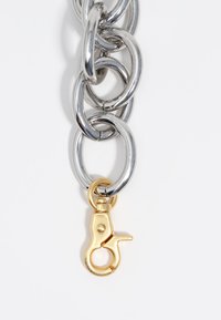Cadena de metal plateado con grandes anillos entrelazados, con un cierre de langosta de color dorado en el extremo. Textura suave, acabado pulido.