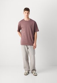 T-shirt de crew neck vinho em algodão suave, combinada com jeans baggy cinza claro e ténis com pormenores verdes. Ajuste simples e boxy.