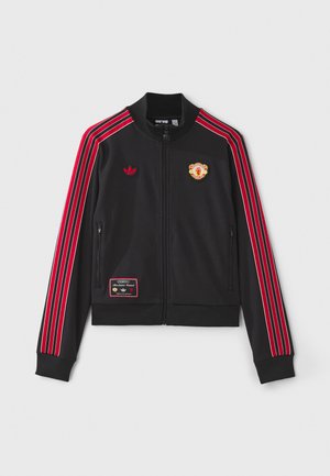 Zwarte zip-up jas met rode strepen langs de mouwen, geborduurd logo op de borst en een patch op de linker onderkant. Zachte stof.
